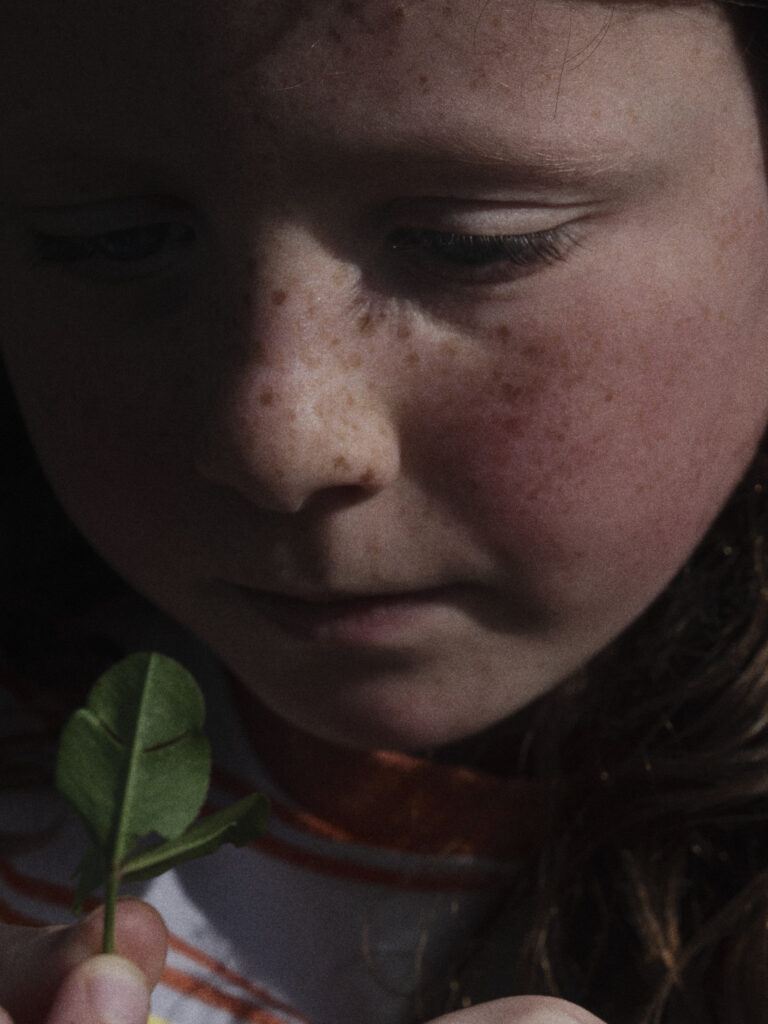 A child looking down at a small green leaf held up to their chin