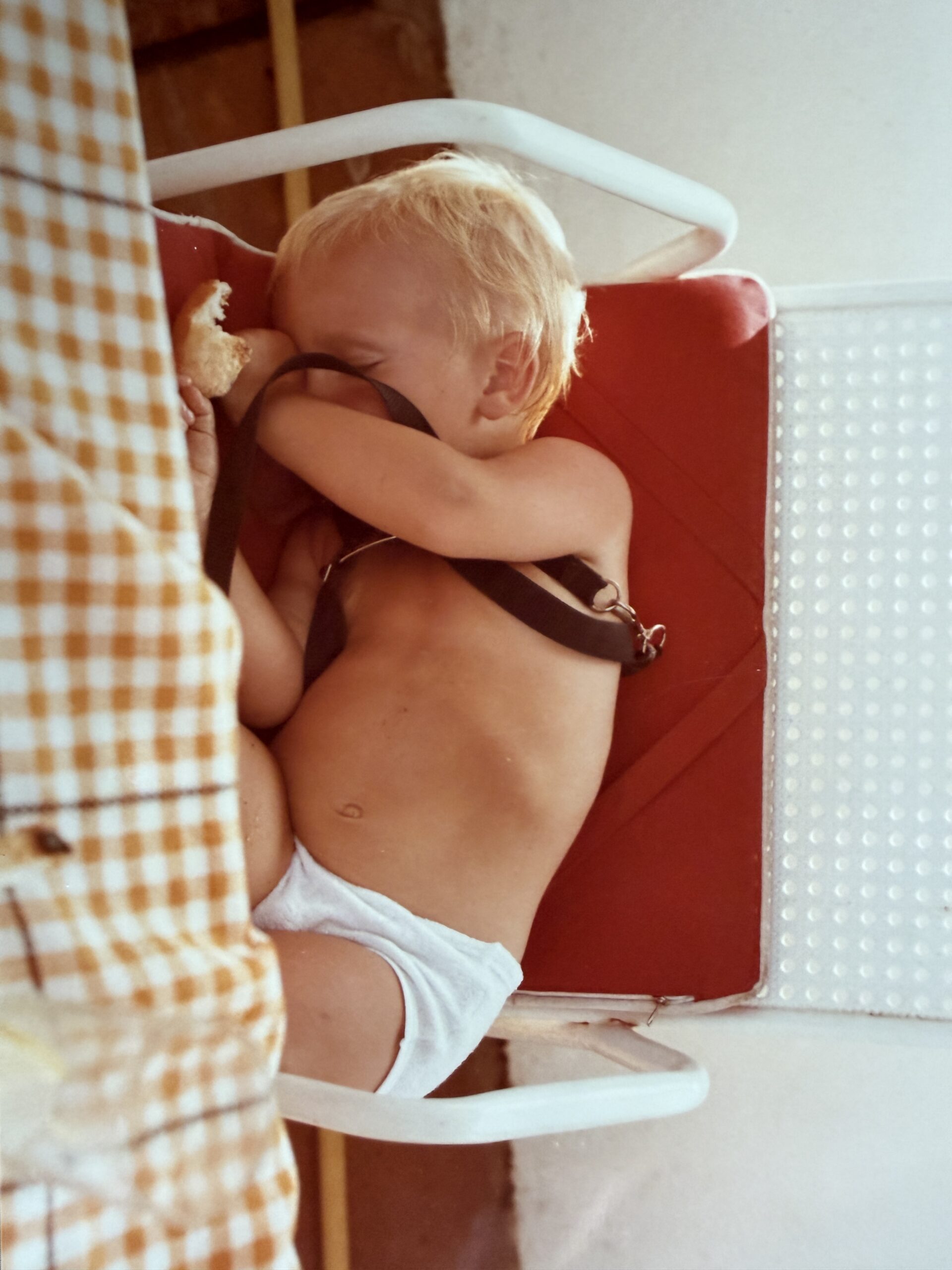 A baby strapped into a high chair beside a checked curtain