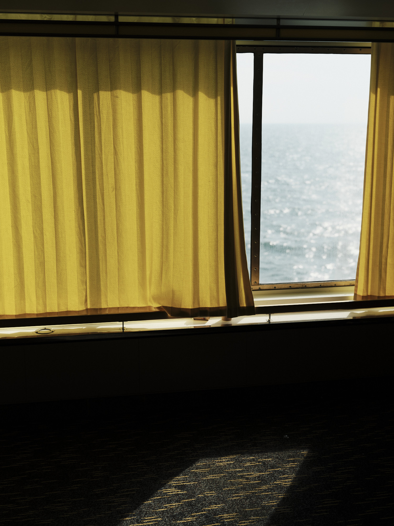 A ferry window with a yellow curtain drawn back to the sea