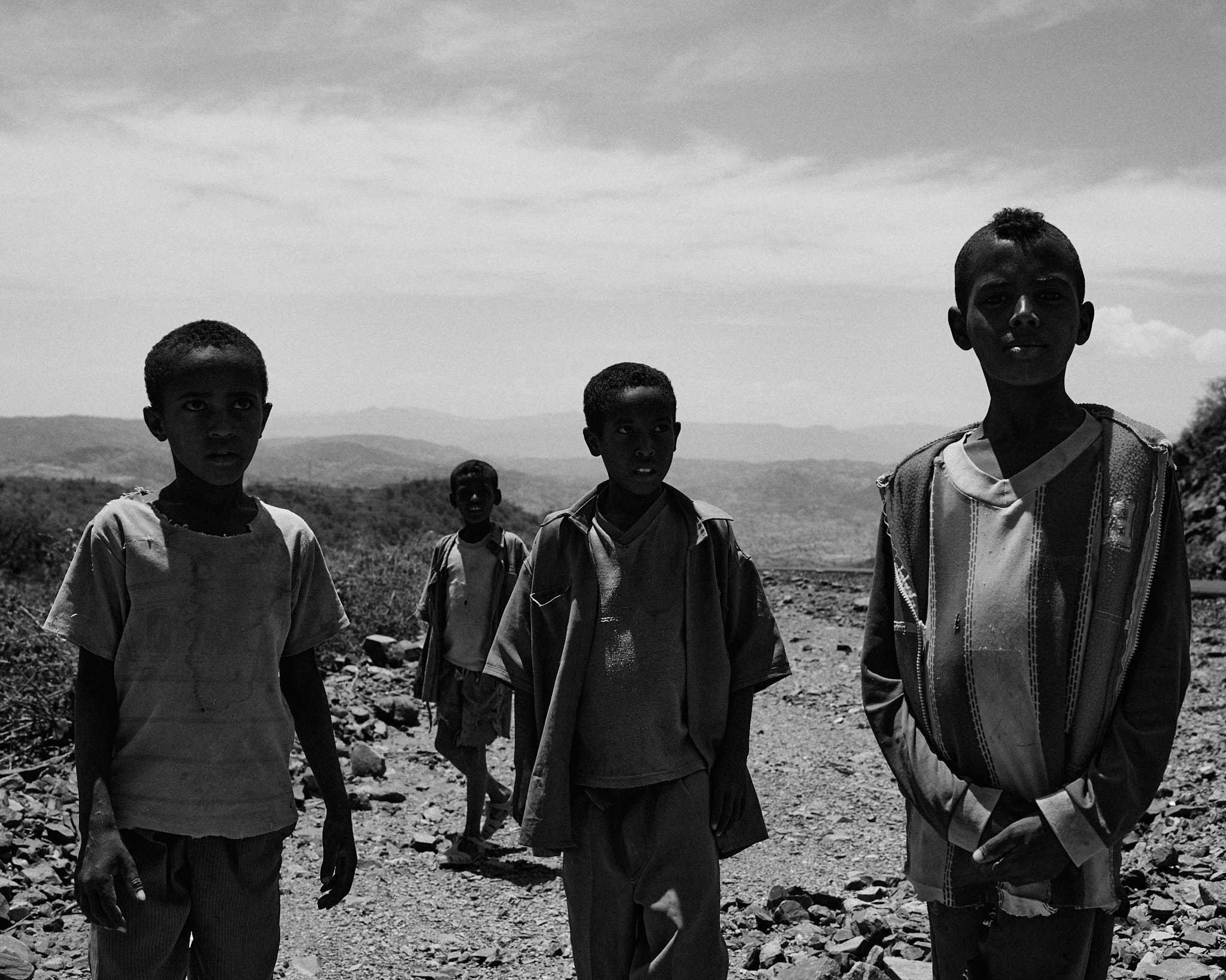Four young men standing together on a stony path in open country