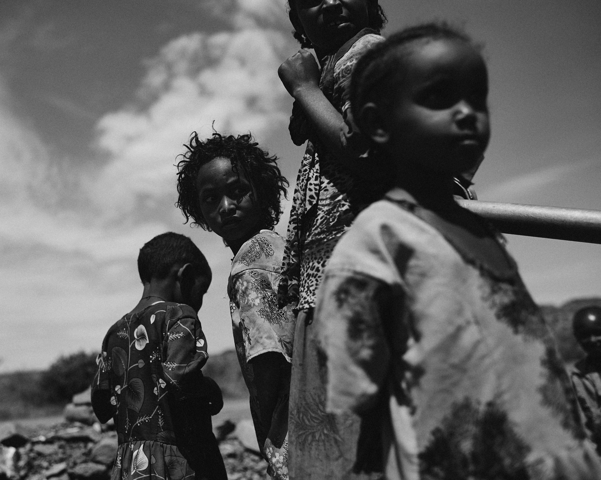 A group of children standing close together outdoors, one looking to camera