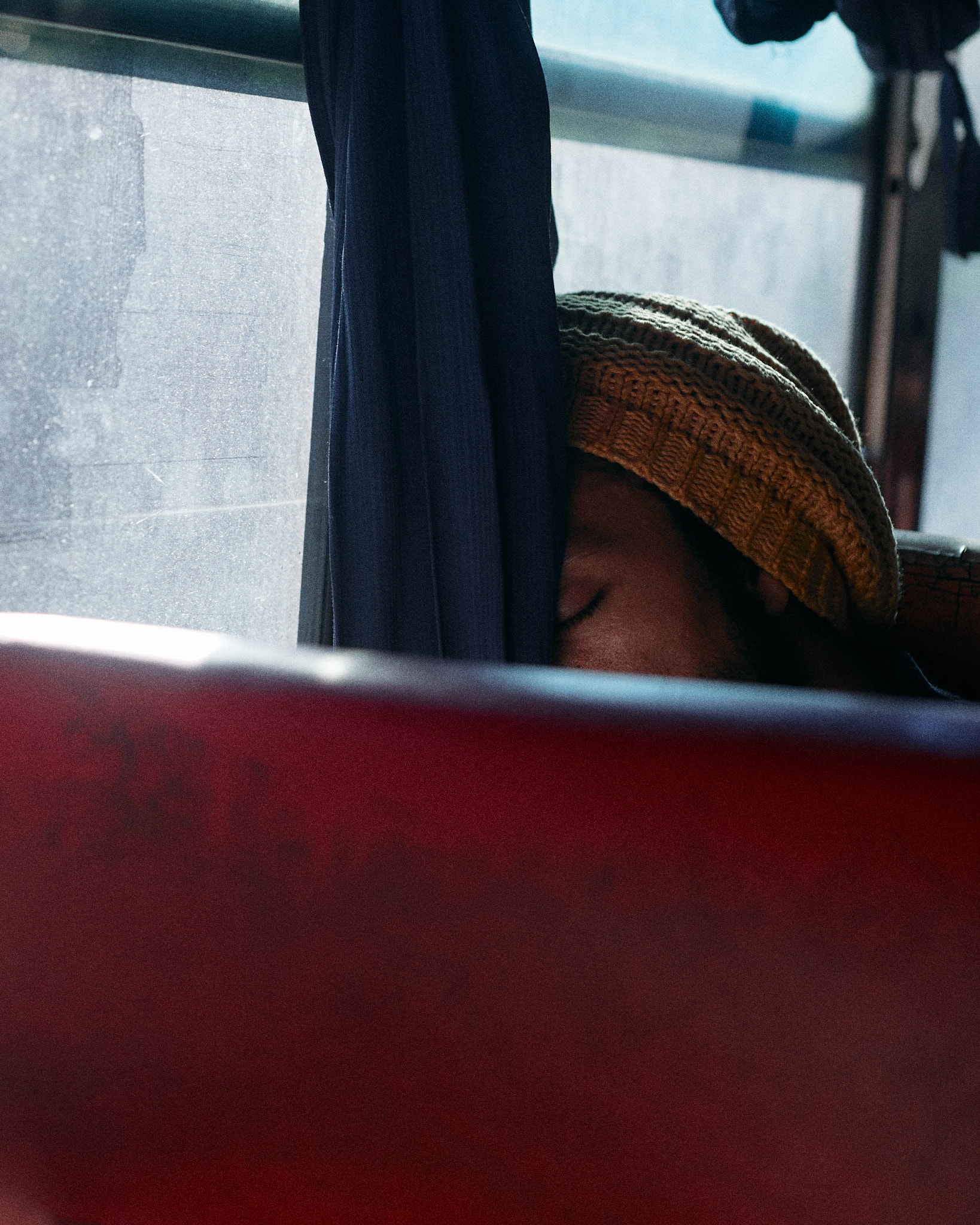 A passenger in a cap just visible above a red bus seat