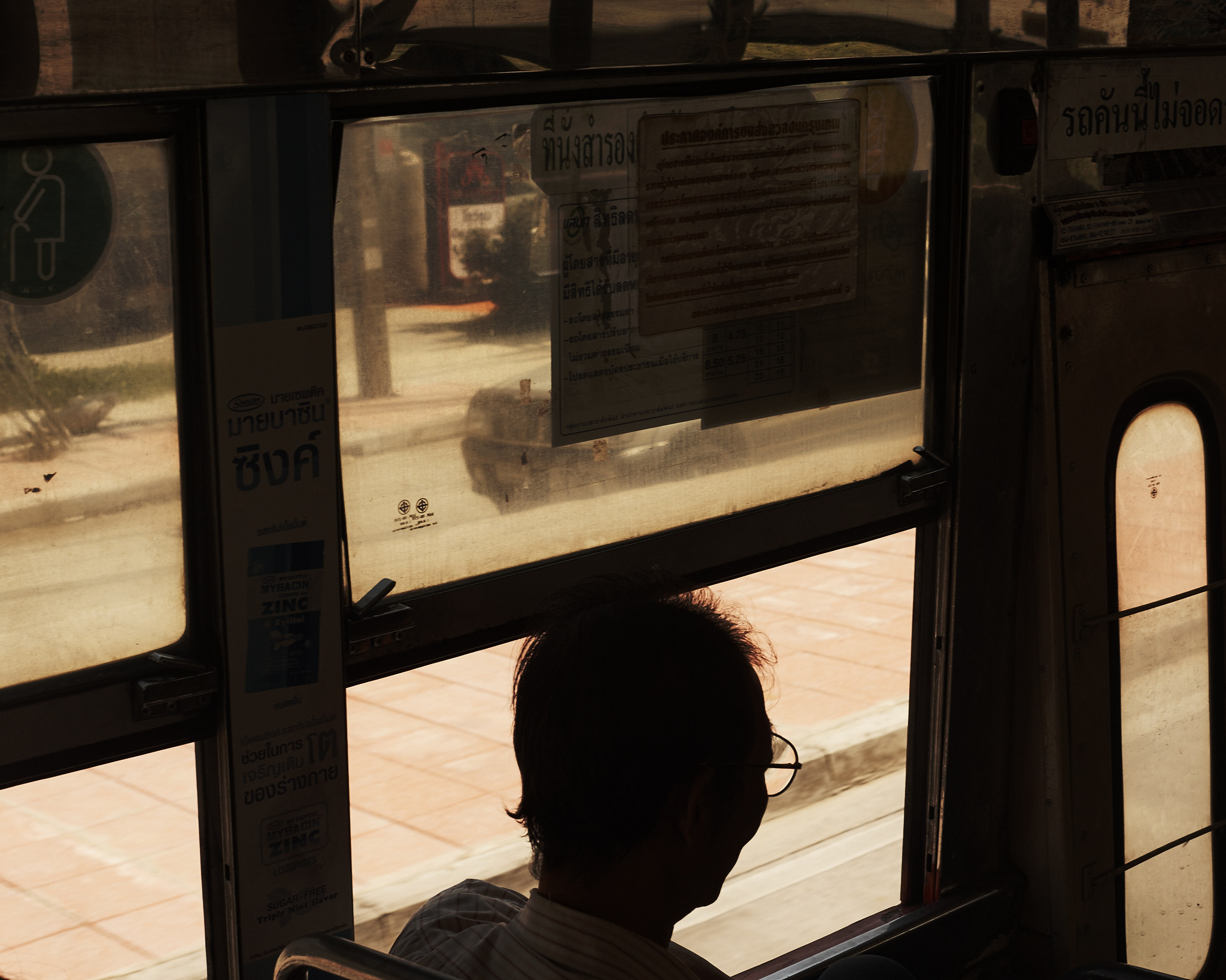 A passenger silhouetted against a bus window with the street outside