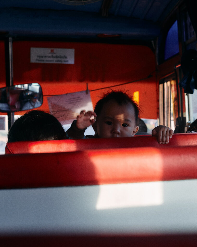 Passengers in red bus seats with sunlight falling across the seat backs
