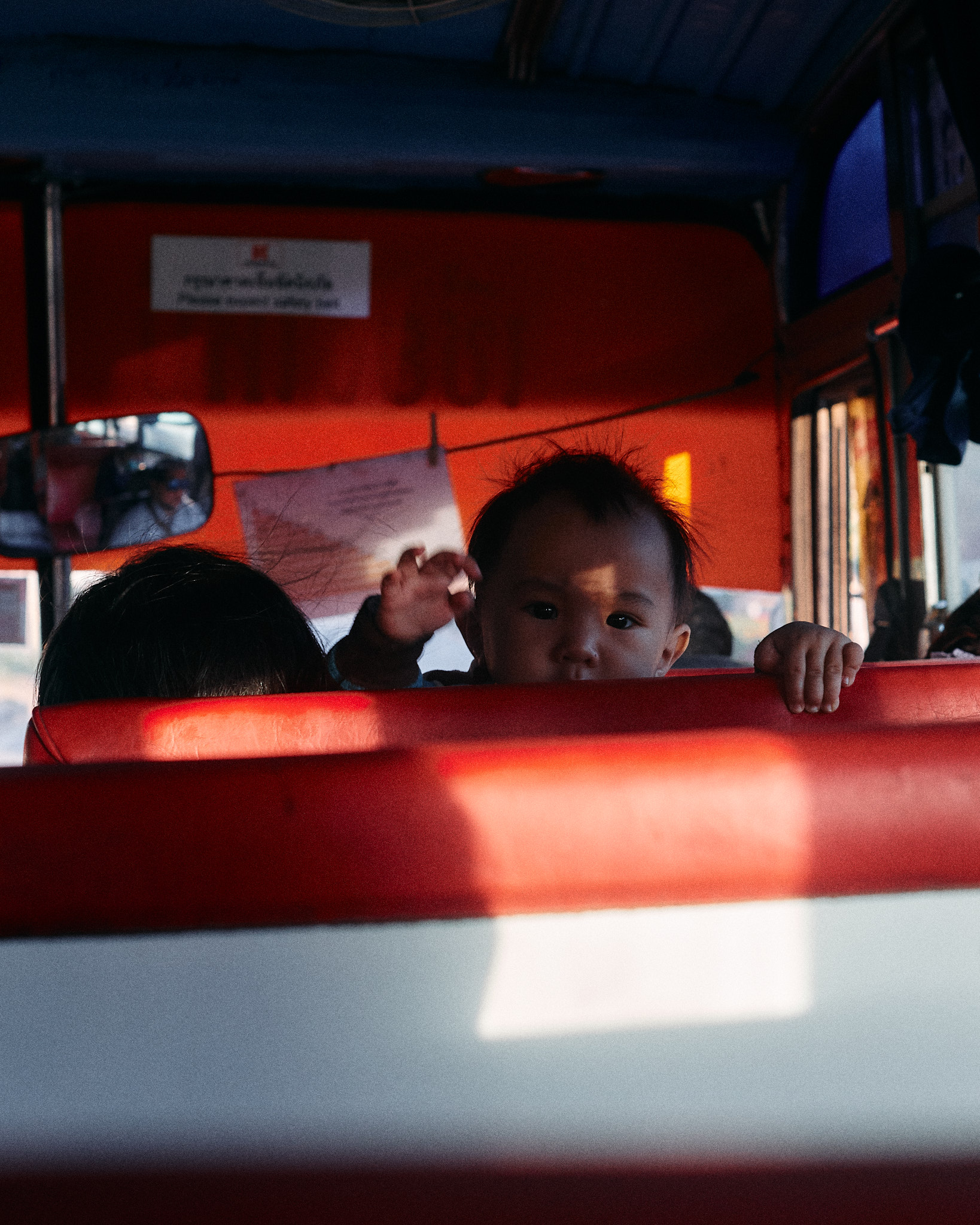 Passengers in red bus seats with sunlight falling across the seat backs