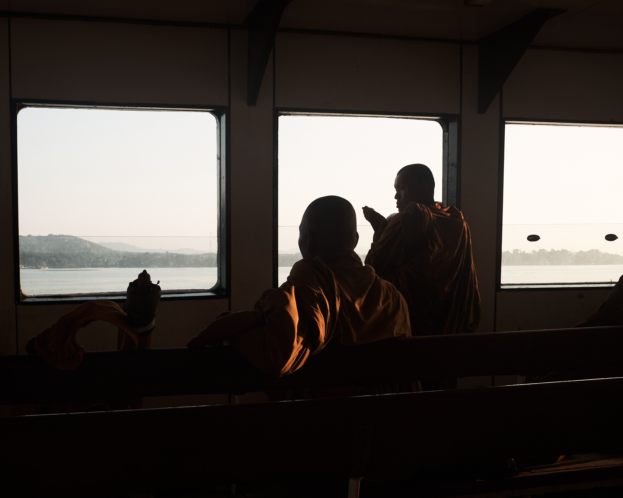 Passengers silhouetted against the windows of a boat looking out over water