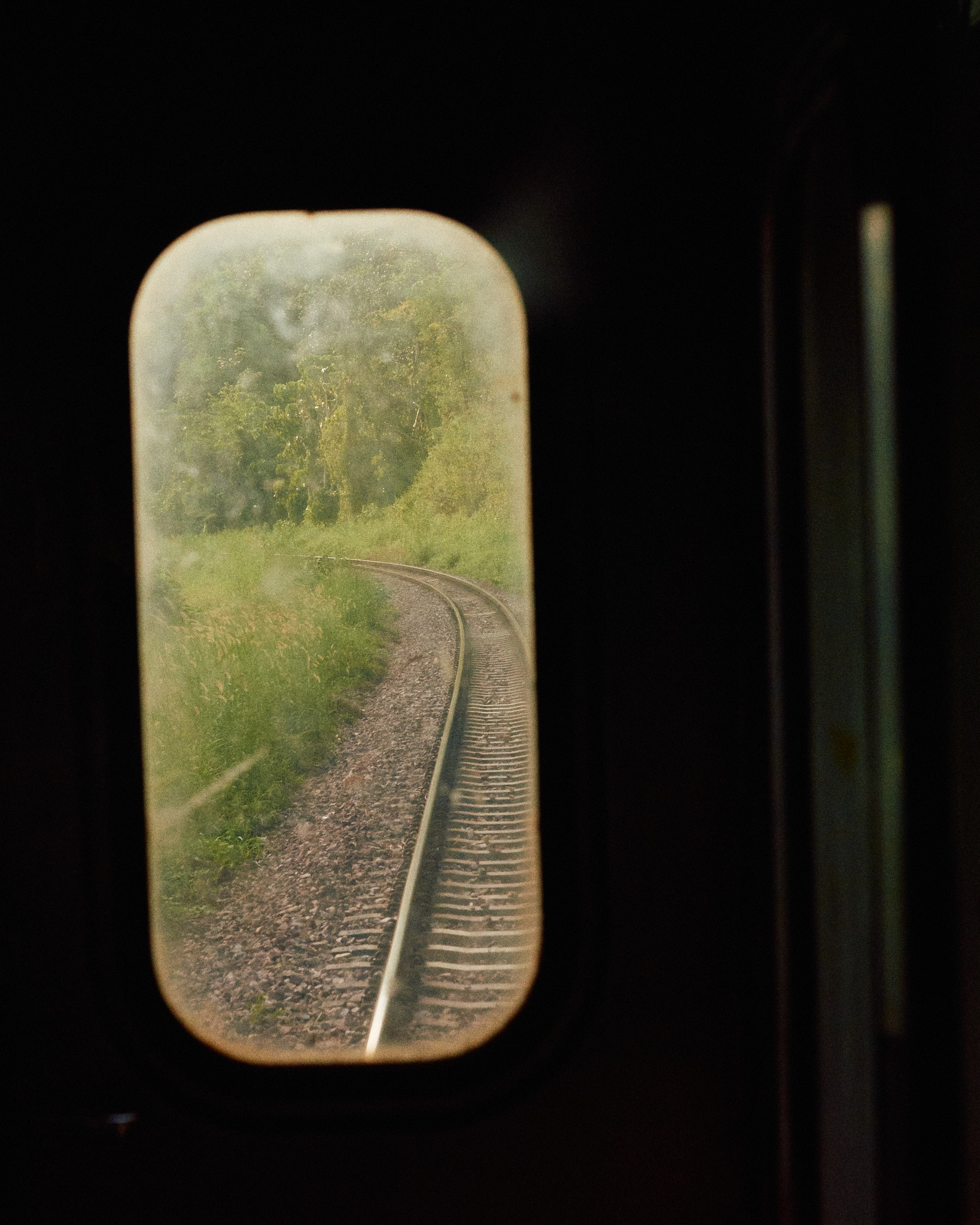 A railway track receding through green countryside, seen from a train window