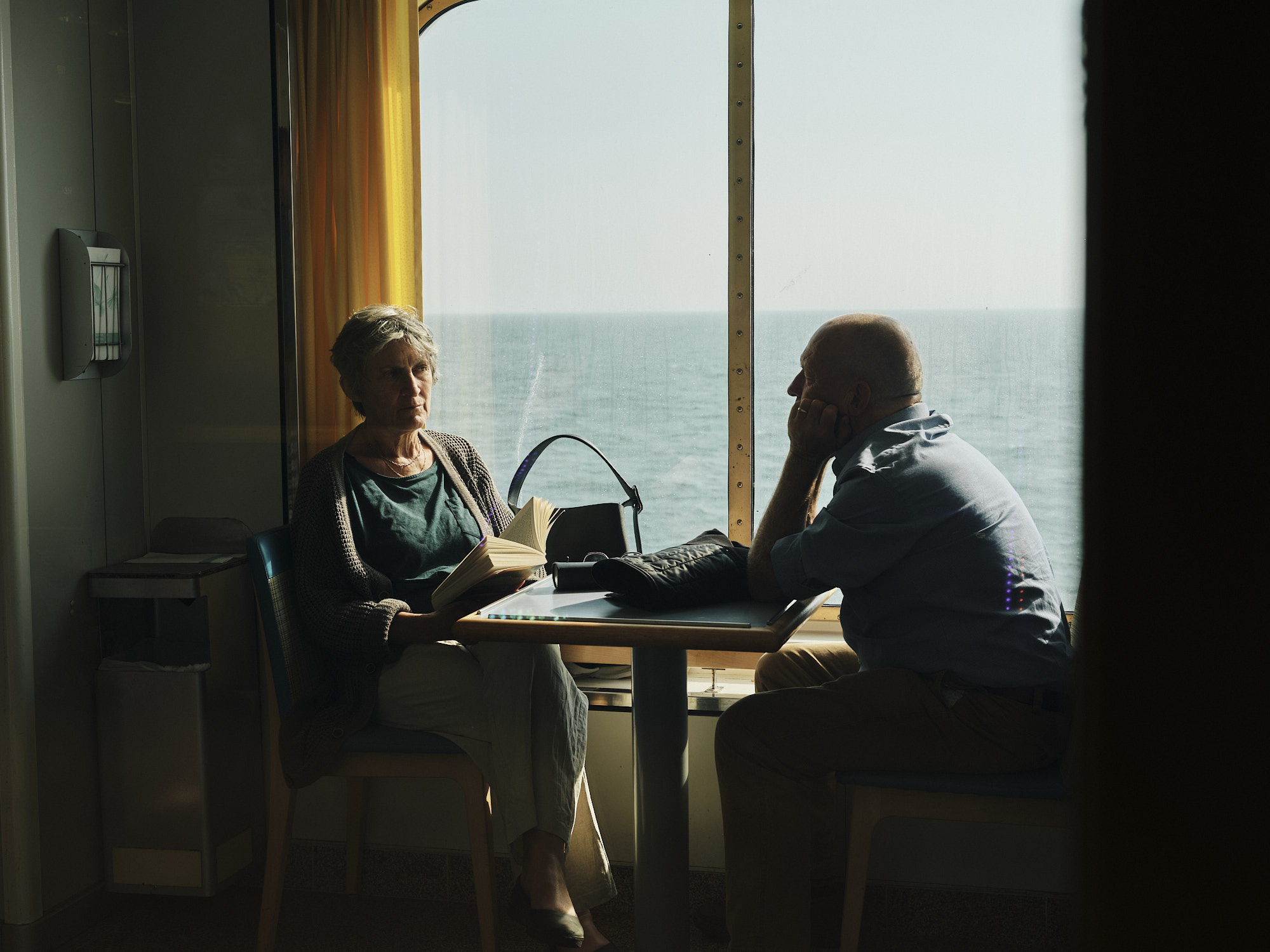 Two people sitting at a table on a ferry, the sea through the window