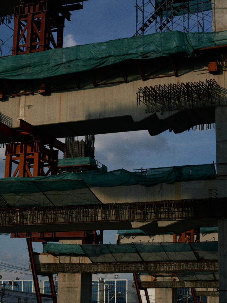 The underside of an elevated road, green netting and red scaffolding above