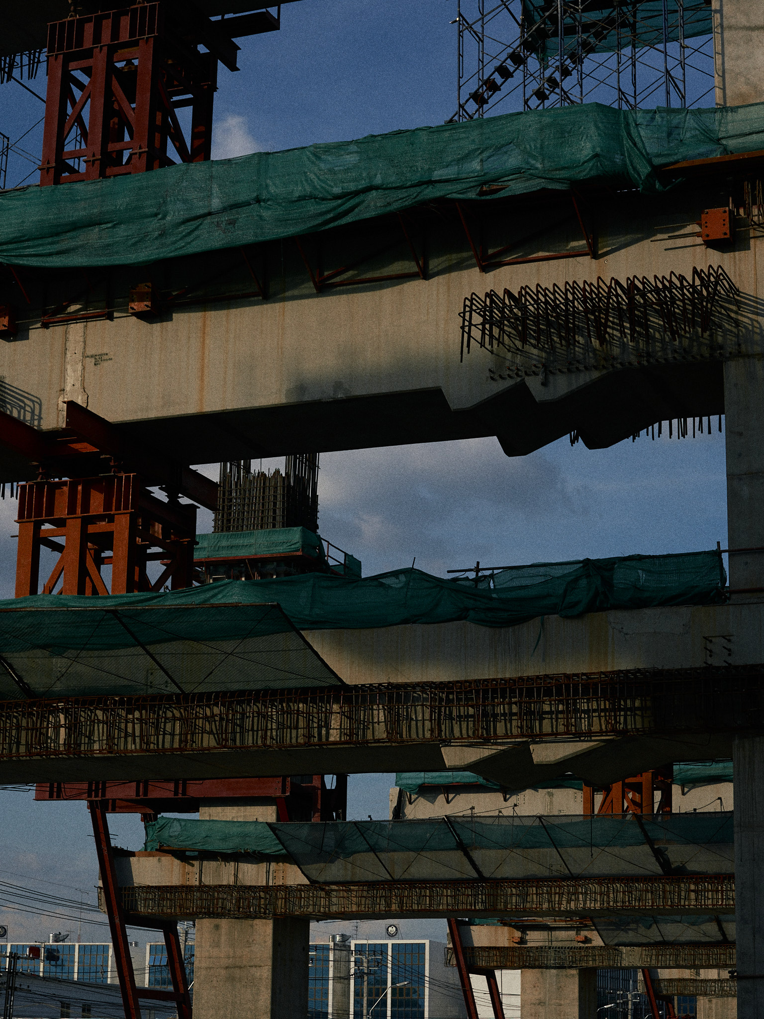 The underside of an elevated road, green netting and red scaffolding above