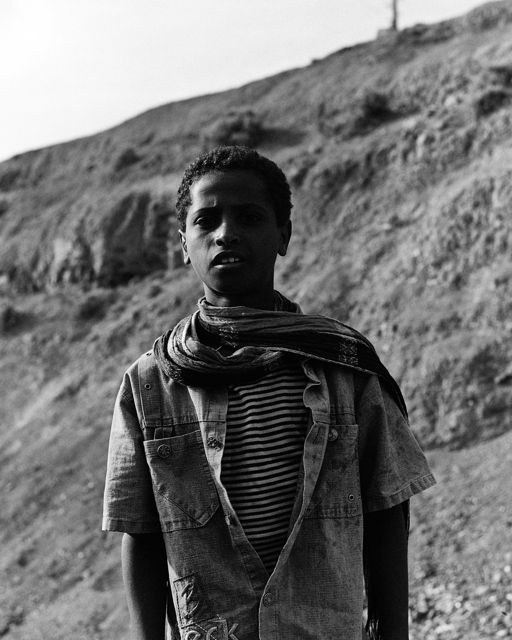 A young person in a patterned scarf standing on a bare hillside